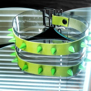 May include: A clear plastic belt with a lime green leather band and silver buckle. The band is studded with lime green spikes.