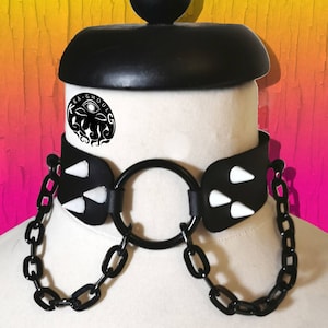 May include: Black leather choker with a large black ring and white spikes. The choker is attached to a black chain.