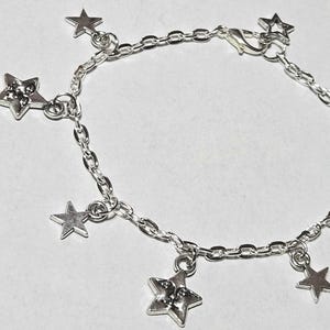 May include: A silver chain bracelet with five dangling star charms. The bracelet has a lobster clasp closure.