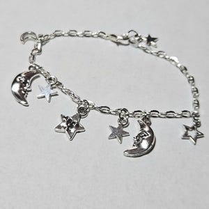 May include: A silver chain bracelet with multiple charms, including crescent moons and stars.