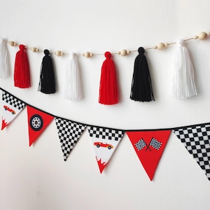 Puede incluir: Una guirnalda festiva con borlas y banderines rojos, negros y blancos. Los banderines presentan un patrón de cuadros, coches de carreras y banderas a cuadros. Cuentas de madera unen las borlas, creando una decoración festiva.