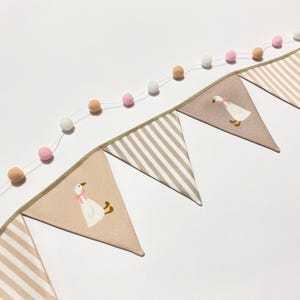 Può includere: Ghirlanda decorativa con bandierine a righe beige e bianche alternate e bandierine con un'illustrazione di oca. Una ghirlanda di pompon rosa, beige e bianchi è sopra. Ideale per una cameretta.
