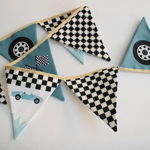 Puede incluir: Un banderín festivo con diseños de carreras. Los banderines triangulares muestran un coche azul claro, banderas a cuadros y patrones de cuadros blancos y negros. El banderín está bordeado con un borde dorado.