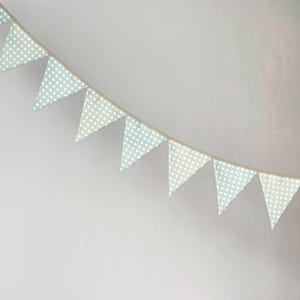 Op de afbeelding: Een decoratieve vlaggenlijn bestaande uit een reeks driehoekige vlaggetjes opgehangen aan een dun koord. Elke vlag heeft een licht saliegroen en wit vichy-ruitpatroon, wat een herhalend geometrisch raster vormt over de gehele lengte.