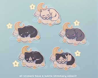 May include: A collection of cat stickers, each featuring a sleeping cat on a cloud with a crescent moon and stars. The cats are in various colors: white, black, gray, and black and white. The stickers have a subtle shimmery effect.