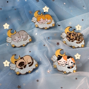 May include: Five enamel pins featuring cartoon cats sleeping on clouds with a crescent moon. The cats are orange, gray, brown and white, calico, and Siamese. Each pin has a gold finish and is numbered 1 through 5.