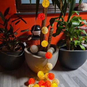 Könnte beinhalten: Eine Lichterkette mit gelben und orangefarbenen Papierkugeln als Glühbirnen. Die Lichter hängen an einer Topfpflanze.