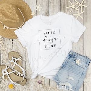 May include: White t-shirt with a black square and the text "YOUR design HERE" on a wood background with a straw hat, denim shorts, and seashells.