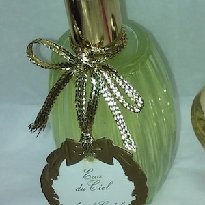 May include: A clear glass bottle of Annick Goutal Eau du Ciel perfume with a gold spray top and a gold ribbon tied around the neck. The bottle has a gold label with the text "Eau du Ciel Annick Goutal Paris".