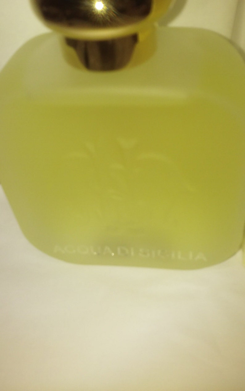May include: A clear glass bottle with a gold cap and a white label that reads "Acqua di Sicilia".