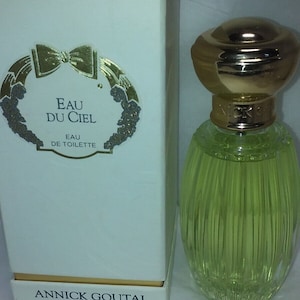 May include: A white box with gold lettering and a gold bow on the front. The box contains a clear glass bottle of perfume with a gold cap. The bottle is labeled "Eau du Ciel" and "Annick Goutal" and contains 3.4 fl oz or 100 ml of perfume.