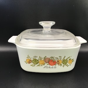 May include: White square casserole dish with a glass lid. The dish has a green and brown floral design with a variety of vegetables and the text "L'Echalote".