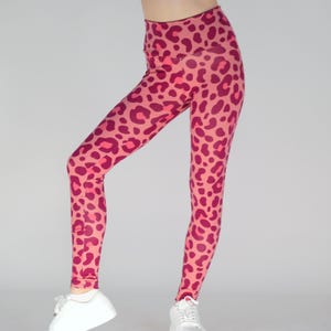 Könnte beinhalten: Pinkfarbene Leggings mit magenta Leopardenmuster. Die Leggings haben einen hohen Bund und eine enge Passform. Das Leopardenmuster wiederholt sich über die gesamte Leggings. Die Leggings bestehen aus einem dehnbaren Material.