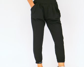Puede incluir: Pantalones negros de cintura alta con una cinturilla ancha y bolsillos. Los pantalones tienen un corte holgado en las caderas y se estrechan en los tobillos. La modelo lleva tacones plateados con tiras. Los pantalones son de tejido suave y fluido.