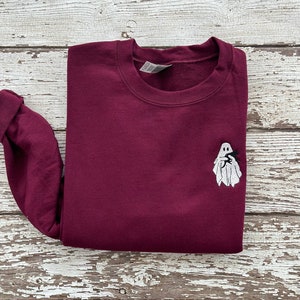May include: A maroon sweatshirt with a white ghost embroidered on the front. The ghost is holding a small black bat.