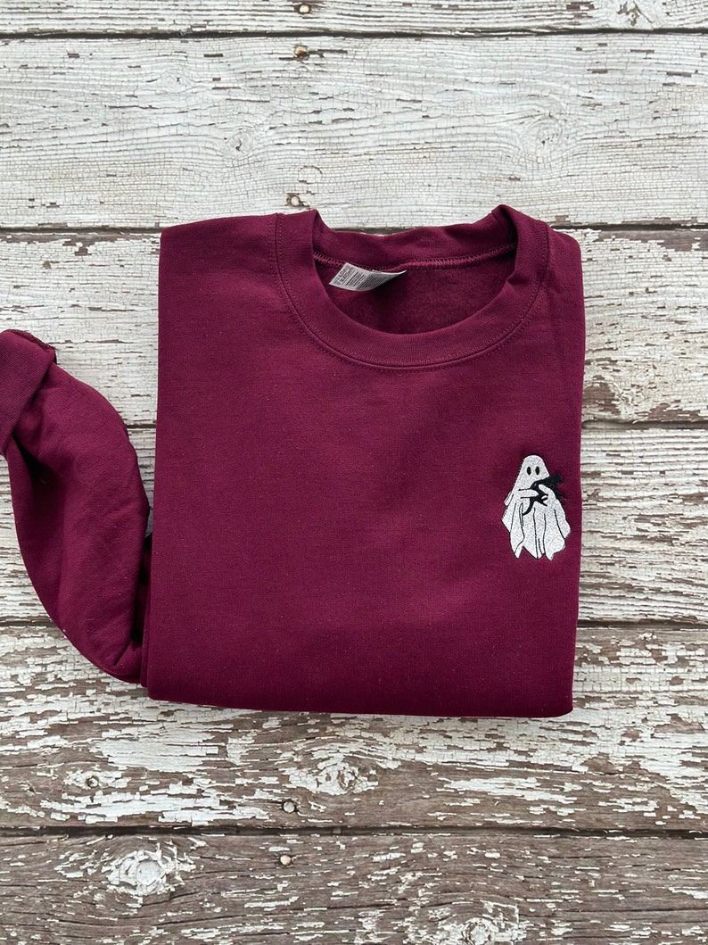 May include: A maroon sweatshirt with a white ghost embroidered on the front. The ghost is holding a small black bat.