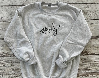 May include: A gray sweatshirt with the word "spooky" written in black cursive with a ghost and spiderweb graphic.