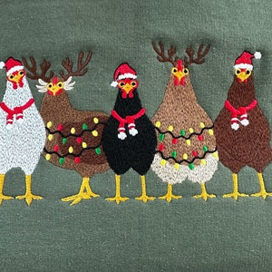 Puede incluir: Cinco pollos de Navidad bordados con gorros de Pap&aacute; Noel rojos y luces de cadena. Los pollos son marrones, blancos y negros.