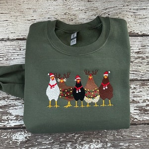 Puede incluir: Un su&eacute;ter navide&ntilde;o verde con un dise&ntilde;o bordado de cuatro pollos con gorros de Pap&aacute; Noel y cuernos de reno. Los pollos est&aacute;n decorados con luces navide&ntilde;as.