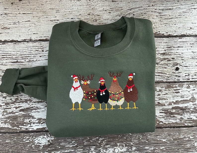 Puede incluir: Un su&eacute;ter navide&ntilde;o verde con un dise&ntilde;o bordado de cuatro pollos con gorros de Pap&aacute; Noel y cuernos de reno. Los pollos est&aacute;n decorados con luces navide&ntilde;as.
