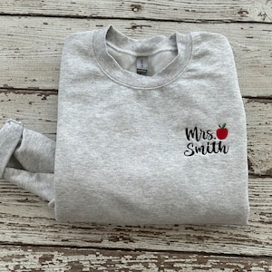 May include: Gray sweatshirt with a black embroidered design that says "Mrs. Smith" with a red apple next to the name.