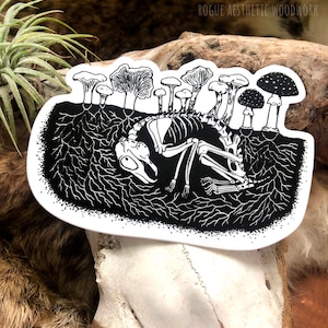 Peut inclure: Autocollant noir et blanc représentant un squelette de petit animal entouré de champignons. L'autocollant est sur fond blanc et a un contour noir.