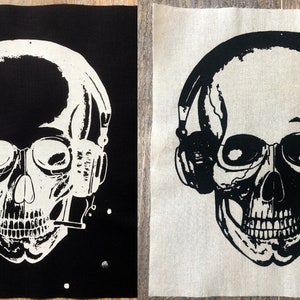 May include: Two black and white fabric patches with a skull wearing headphones and holding a cigarette. The skull is detailed with visible teeth and eye sockets. The patches are on a black and white background.