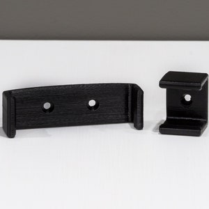 Op de afbeelding: Twee zwarte kunststof wandbeugels met gaten voor schroeven. De beugels zijn ontworpen om een plank of ander object te dragen.