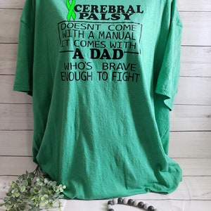 Op de afbeelding: Groen T-shirt met een groen lint en de tekst "Cerebral Palsy Doesn't Come With A Manual It Comes With A Dad Who's Brave Enough To Fight"