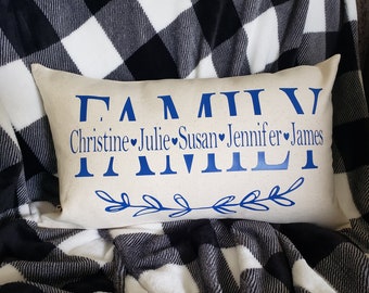 May include: A white throw pillow with the word "FAMILY" spelled out in blue with Roman numerals. The names Christine, Julie, Susan, Jennifer, and James are written below the word "FAMILY" with a heart symbol between each name.