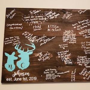 May include: A wooden sign with a light blue deer silhouette and the text "Johnson est. June 1st, 2019". The sign is covered in white handwritten messages of congratulations and well wishes.