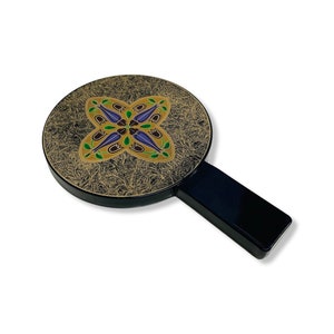 May include: A black hand mirror with a gold and black patterned design. The mirror has a floral design with purple, green, and gold accents.