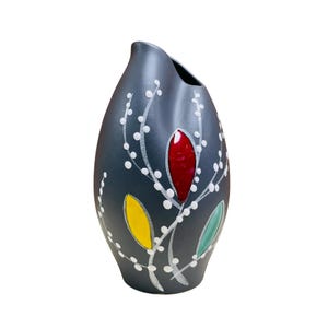 Puede incluir: Un jarrón de cerámica gris oscuro con una forma única y ondulada. Presenta un diseño floral estilizado con ramas blancas, puntos blancos y hojas de colores en tonos rojos, amarillos y verdes.