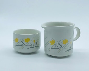May include: A white ceramic creamer and sugar bowl set with a yellow floral pattern on a white background.