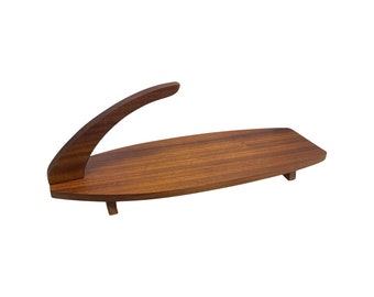 May include: A mid-century modern wooden serving tray with a curved handle. The tray is a warm brown color and has a long, oval shape. It is supported by small wooden feet.