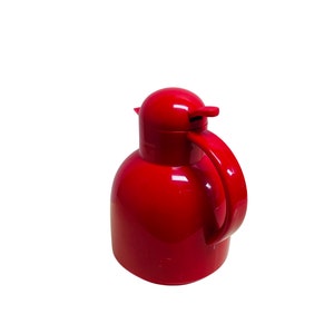 May include: A red thermal carafe with a handle and a pour spout. The carafe is made of plastic and has a glossy finish.