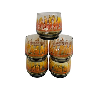 May include: Set of four amber glass tumblers with a pattern of orange and yellow wheat stalks. The glasses are stacked on top of each other.
