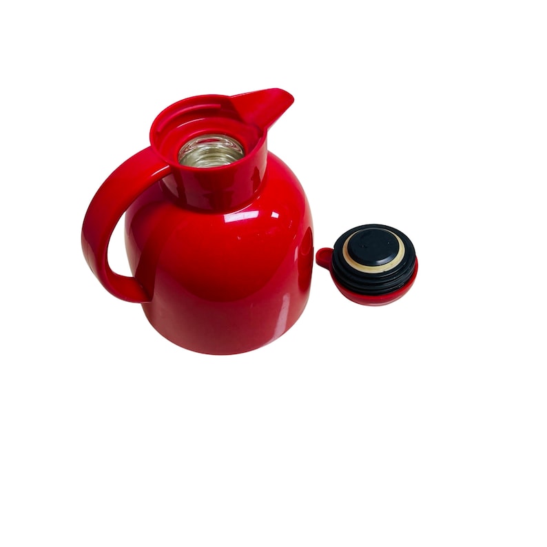 May include: A red thermal carafe with a black lid. The carafe has a handle and a spout. The lid is separate from the carafe.
