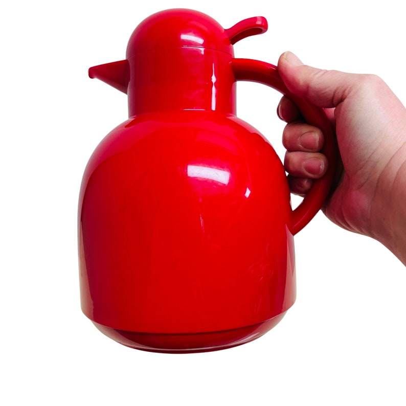May include: A bright red thermos with a bird-shaped handle and lid. The thermos is made of plastic and has a glossy finish.