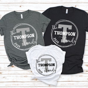 May include: Three t-shirts with a white circle design featuring the text "the Thompson family 2020" and a large gray letter "T". The shirts are in gray, black, and white.