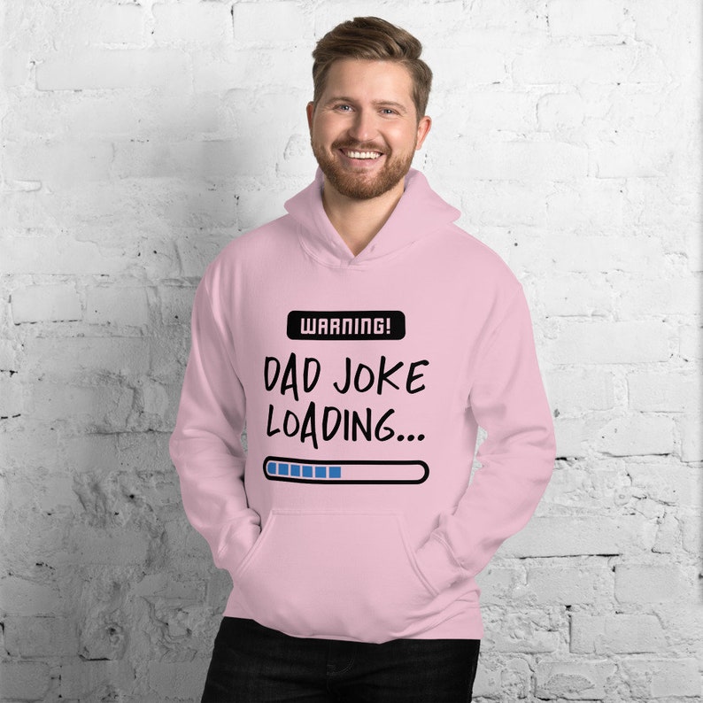May include: A light pink hoodie with a front pocket and a drawstring hood. The hoodie features the text "WARNING! DAD JOKE LOADING..." in black and white, with a loading bar graphic.