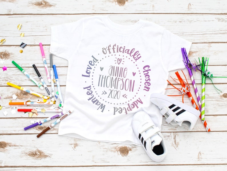 Puede incluir: Camiseta blanca con un dise&ntilde;o circular morado y rosa que dice "Oficialmente Elegido, Deseado, Amado, Adoptado, Annie Thompson, 2020".