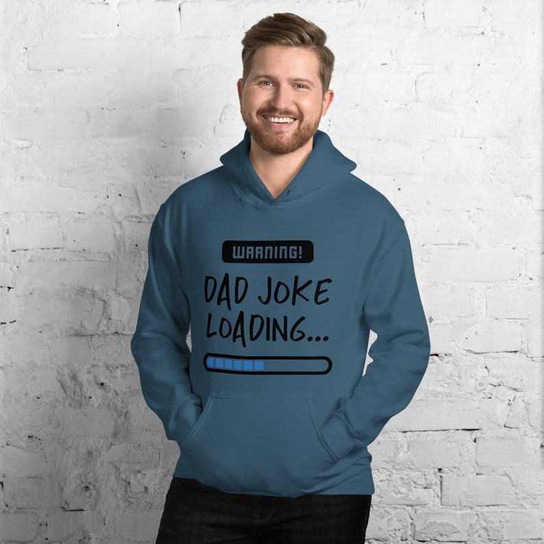 May include: Teal hoodie with a front pocket and a drawstring hood. The hoodie features the text "WARNING! DAD JOKE LOADING..." in black, with a blue progress bar graphic. The hoodie is made of a soft material.
