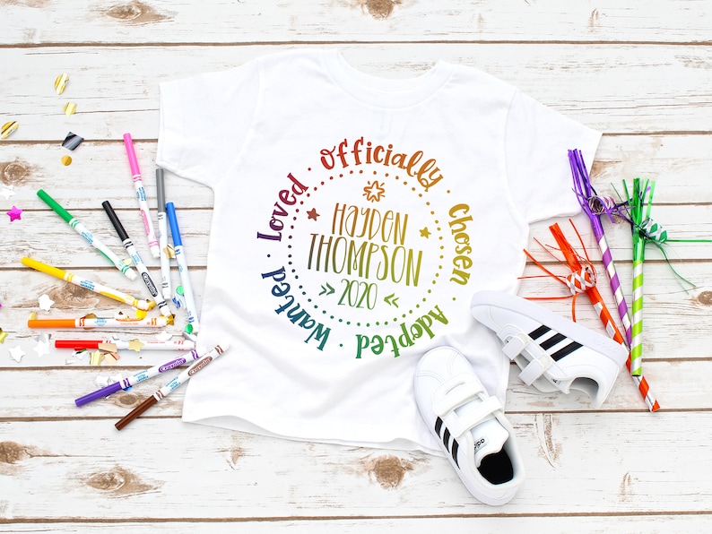 Puede incluir: Camiseta blanca con un dise&ntilde;o circular de arco&iacute;ris que dice "Adoptado oficialmente, elegido, amado, querido" con el nombre "Hayden Thompson" y el a&ntilde;o "2020" en el centro.