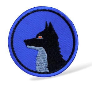 Può includere: Toppa rotonda ricamata con la testa di un lupo nero di profilo su sfondo blu. Il lupo ha un occhio arancione e un petto azzurro. La toppa è bordata da un anello blu scuro.