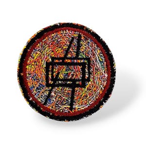 May include: Circular embroidered patch with a black border and a colourful, textured interior. The patch features a black, stylised Japanese character in the centre. The background is a mix of orange, yellow, blue, and red threads.
