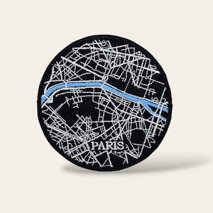 Può includere: Una toppa rotonda nera ricamata con una mappa bianca di Parigi, Francia. Un fiume blu attraversa il centro della mappa. La parola "PARIS" è ricamata in bianco nella parte inferiore.