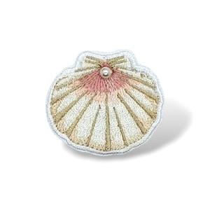 Op de afbeelding: Geborduurde schelpenbroche met een parelaccent. De broche heeft een waaiervormig ontwerp met crème, roze en gouden draad. De randen zijn omrand met lichtblauwe draad. Perfect om een vleugje kustcharme toe te voegen.