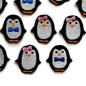 Peut inclure: Dix patchs brodés à repasser en forme de pingouins portant des nœuds papillon et certains avec des nœuds roses. Les pingouins sont blancs avec un bec et des pieds noirs.