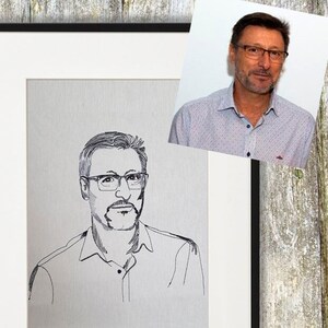 Op de afbeelding: Een zwart-witte lijntekening van een persoon met een bril en een overhemd met kraag. De tekening is ingelijst in een zwart frame.